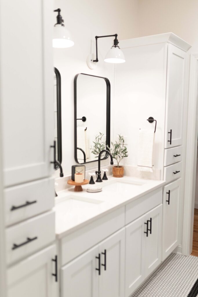 White cabinets in a bathroom with black mirrors and a black and white tile floor. 